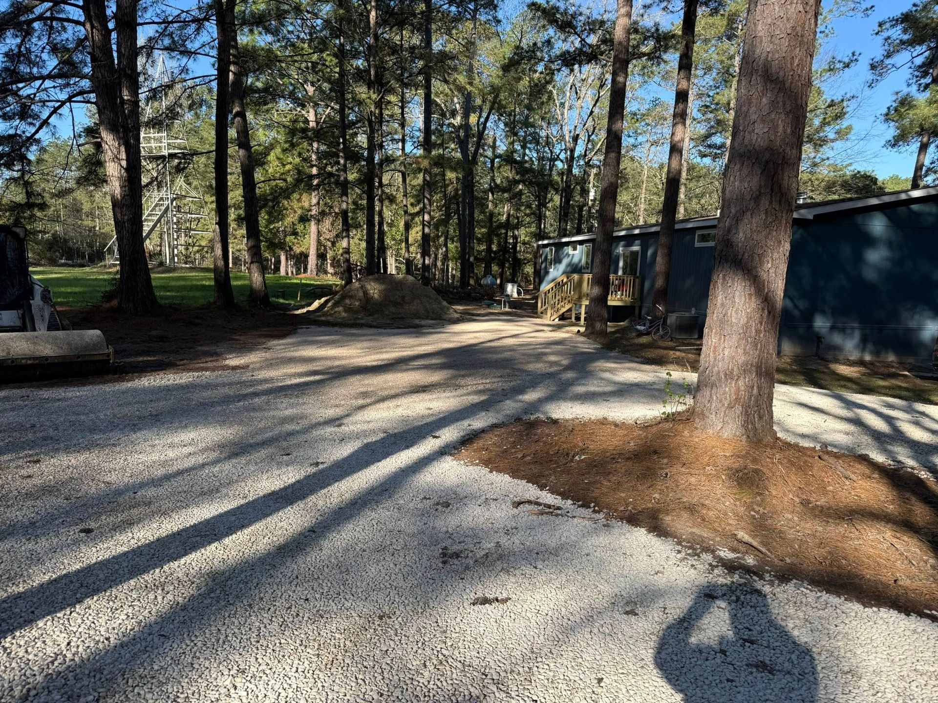 A gravel driveway surrounded by trees and a blue building.