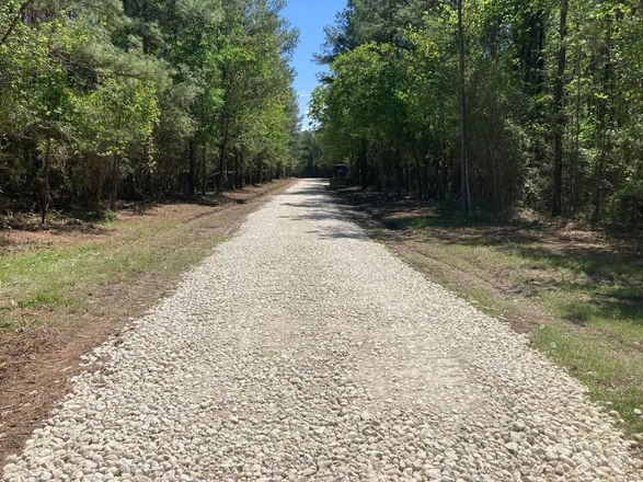 A gravel road going through a forest with trees on both sides.