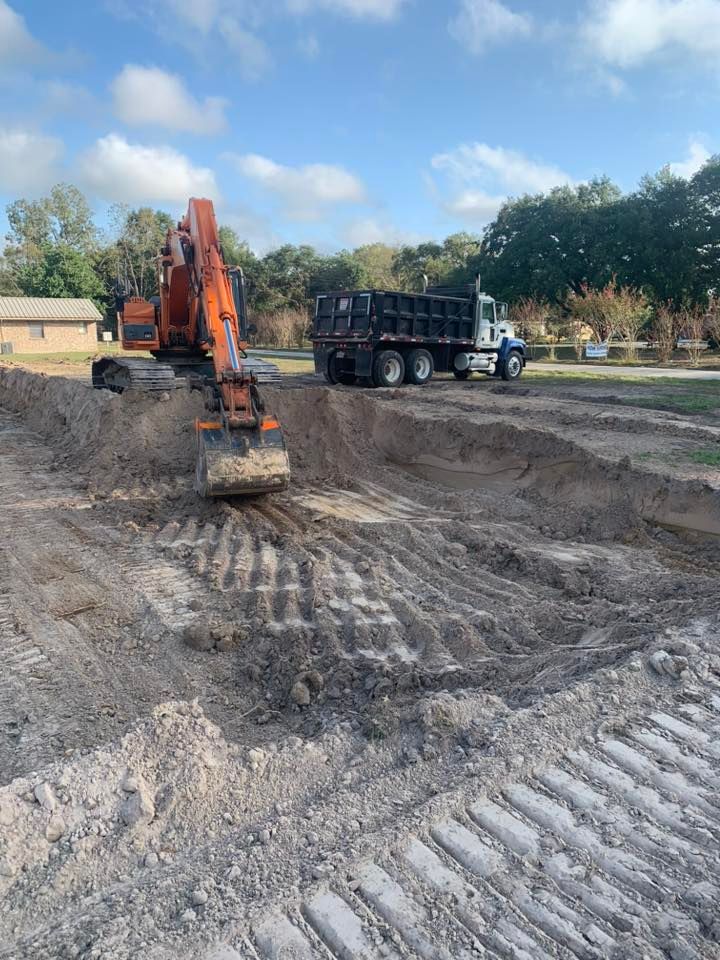 An excavator is digging a hole in the dirt next to a dump truck.