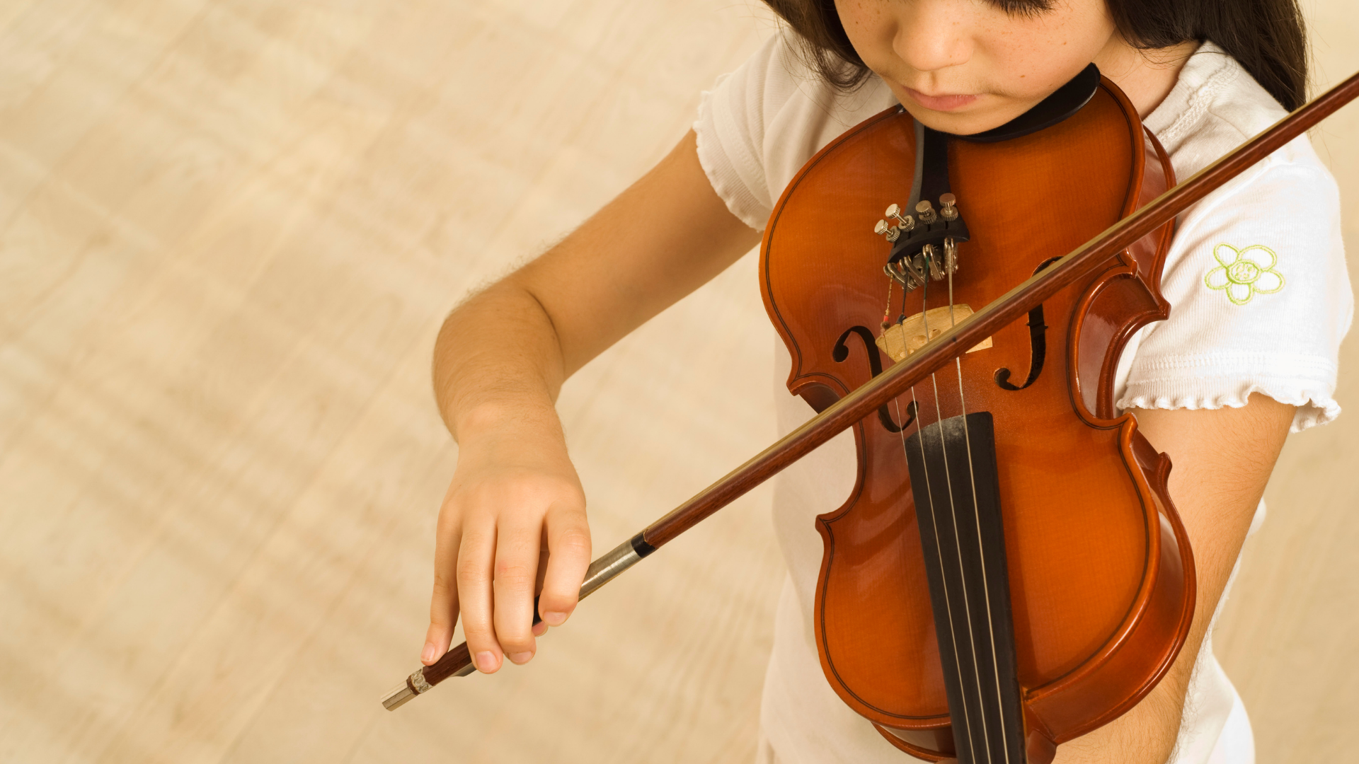 A young girl is playing a violin with a bow.