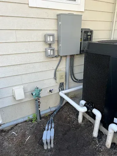 Outdoor electrical boxes and utility pipes beside a house wall, next to an HVAC unit.