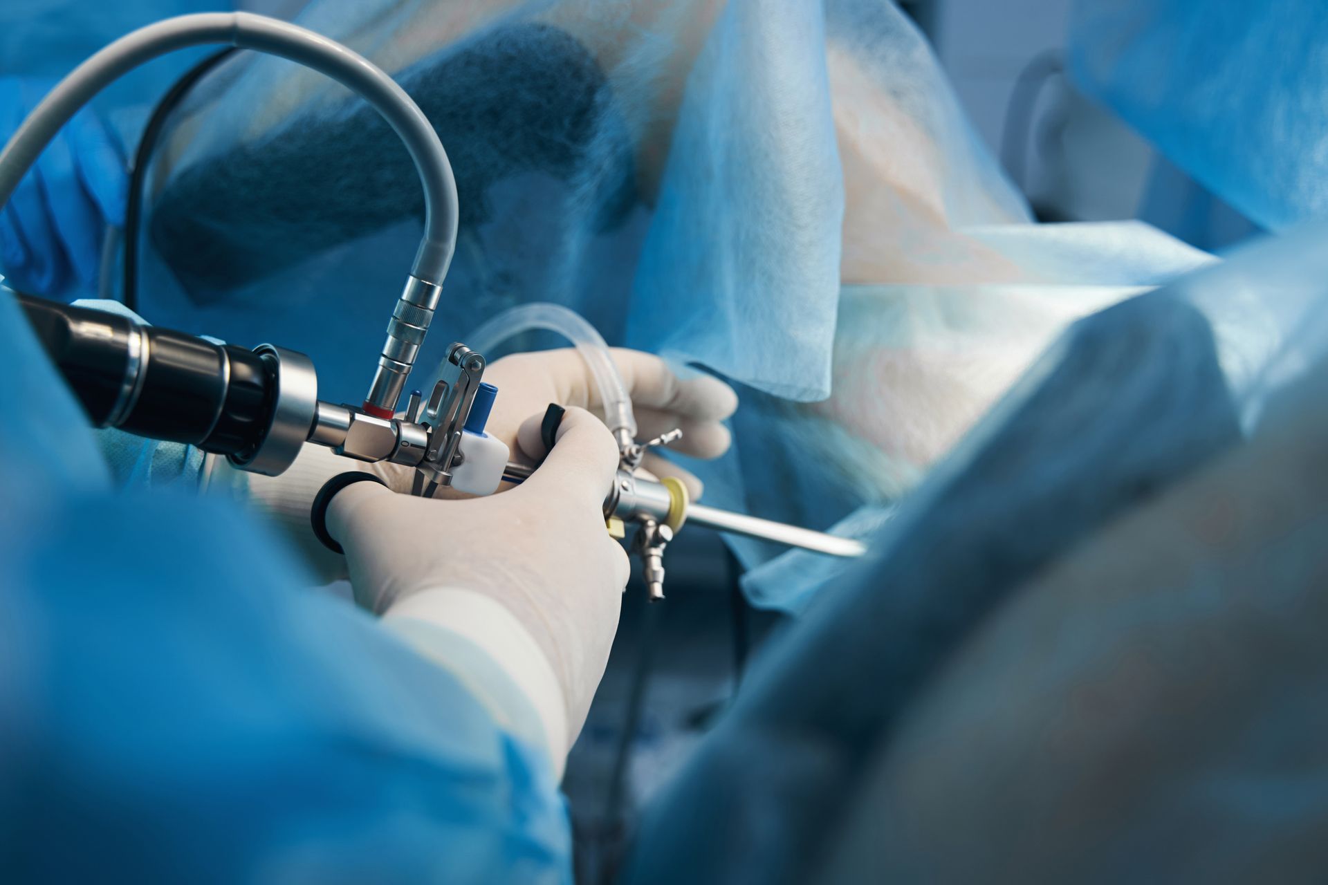 Close-up of a doctor in latex gloves standing with a hysteroscope near the patient.