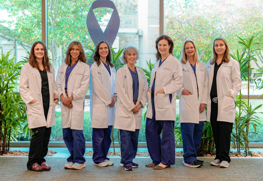 A group of female doctors are posing for a picture in front of a purple ribbon.