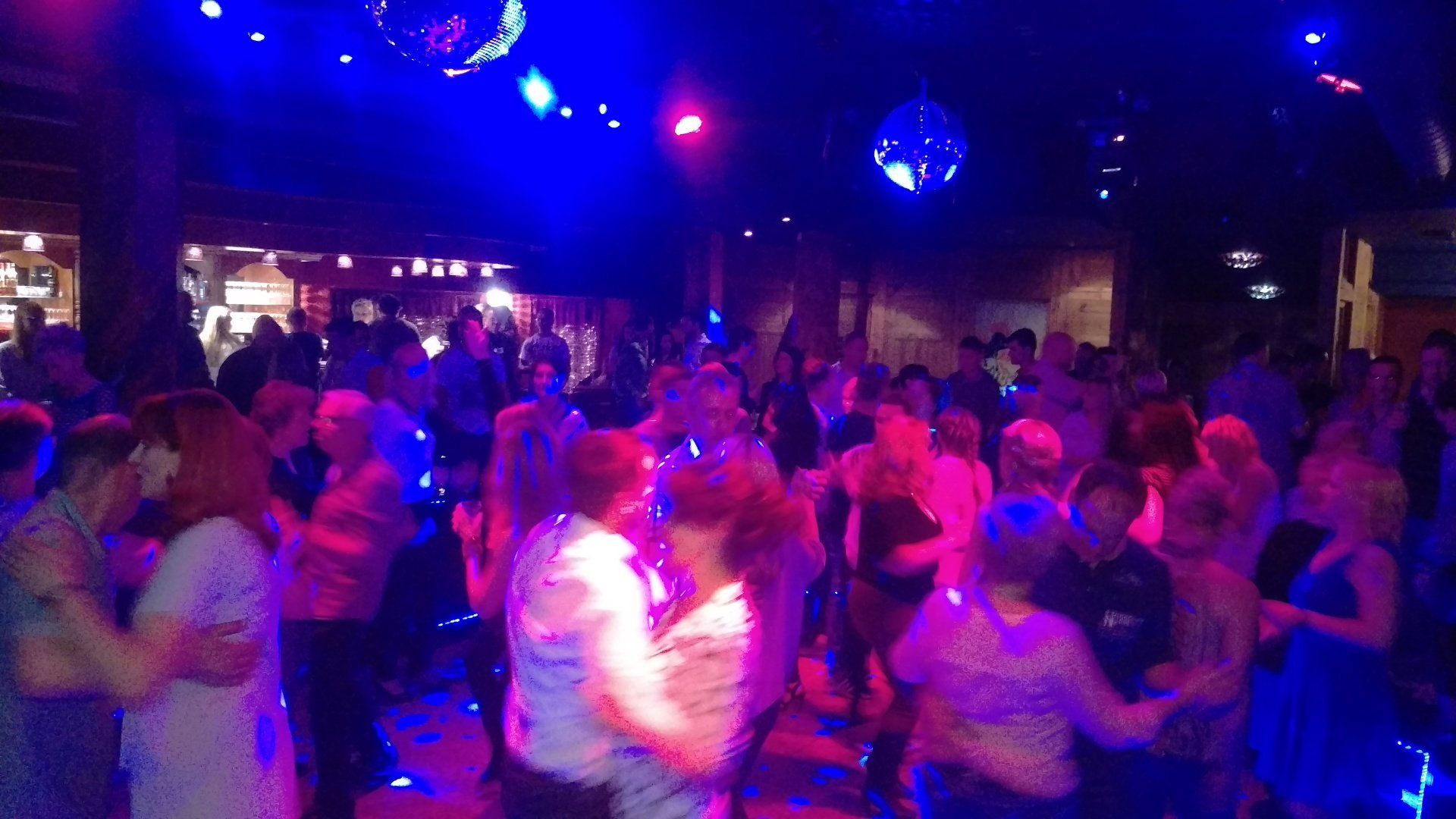 Eine große Gruppe von Menschen tanzt in einem dunklen Raum mit blauem Licht.