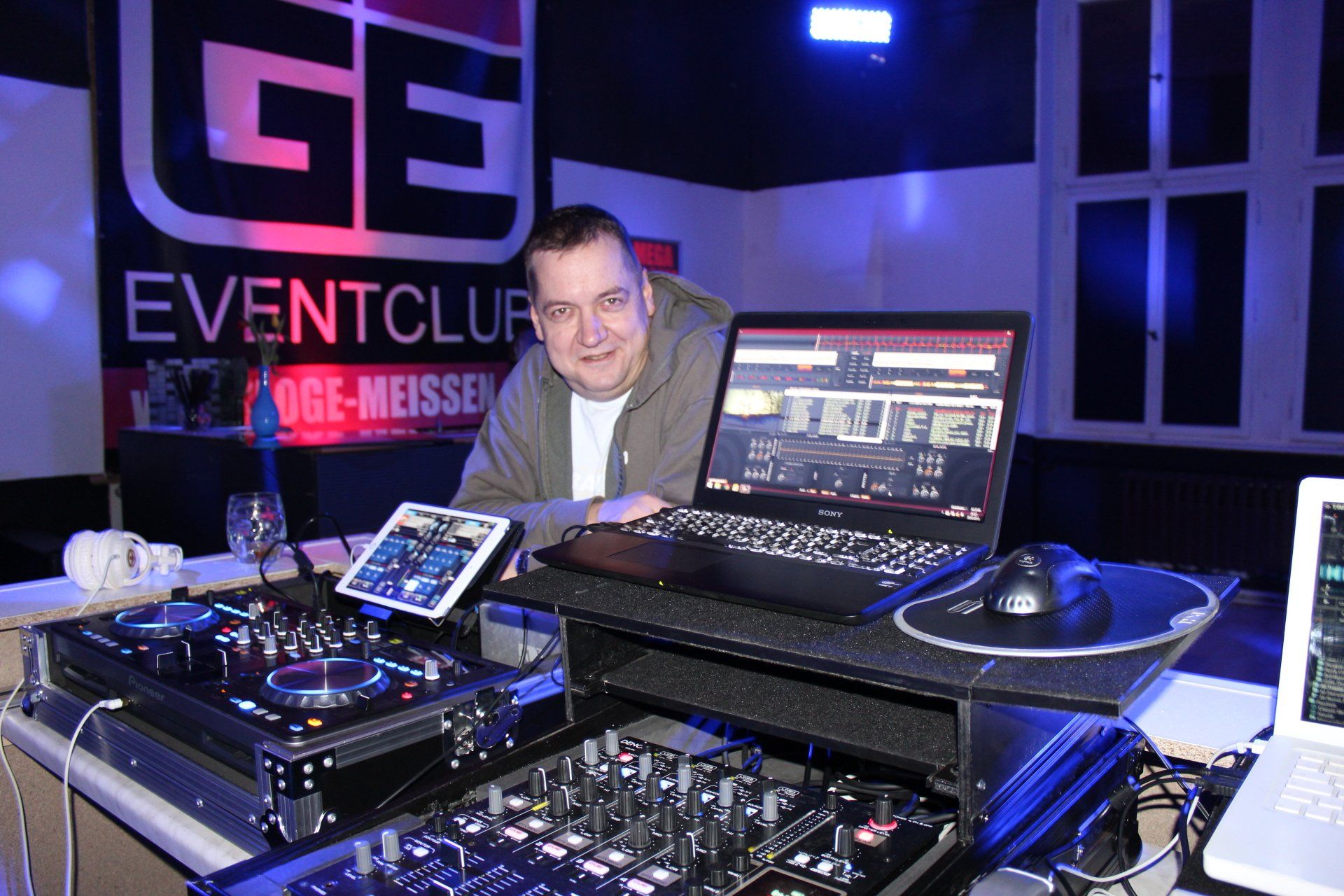 Ein Mann sitzt mit einem Laptop an einem Tisch vor einem Schild mit der Aufschrift „Eventclub“