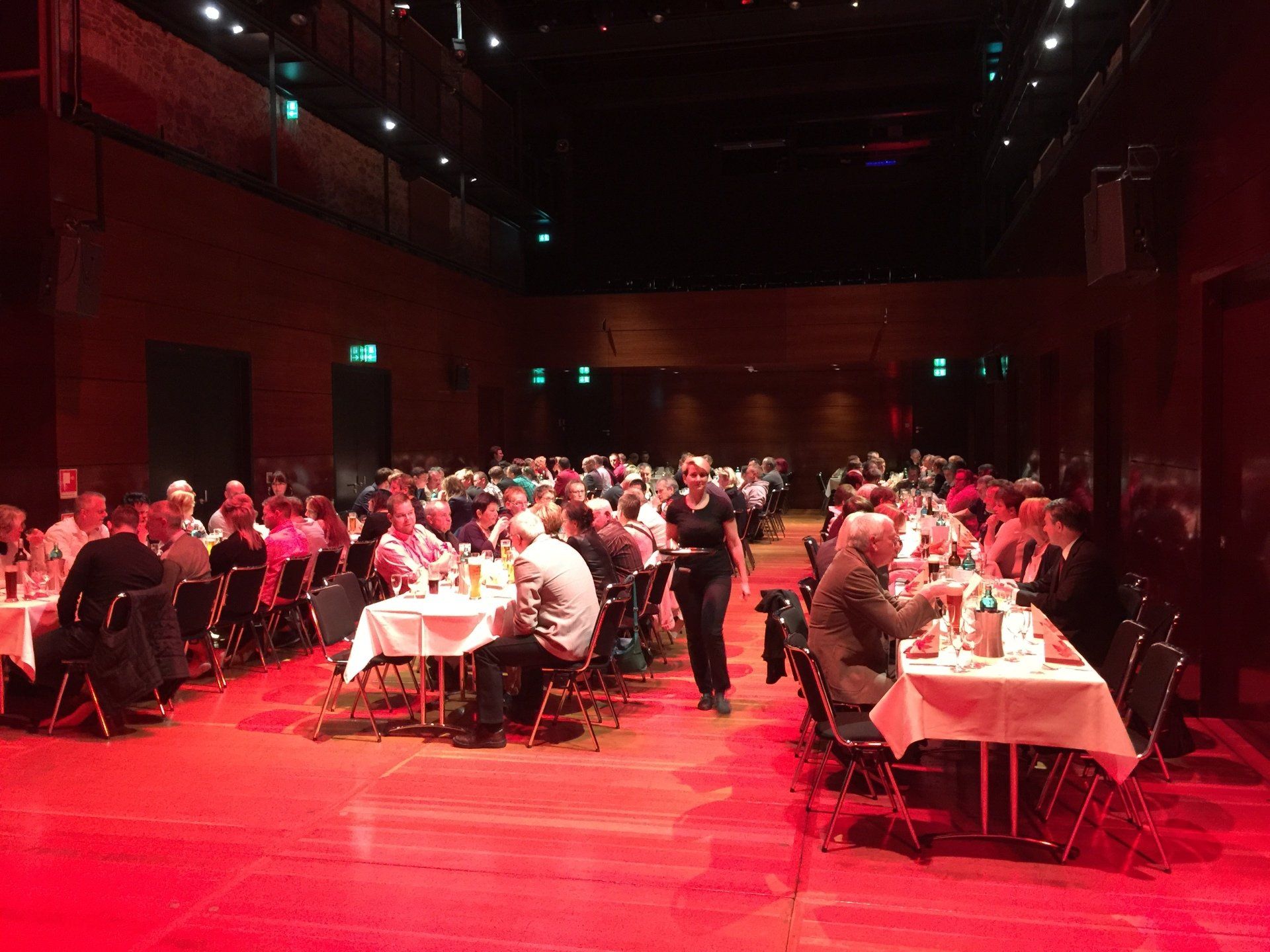 Eine große Gruppe von Menschen sitzt in einem großen Raum an Tischen.