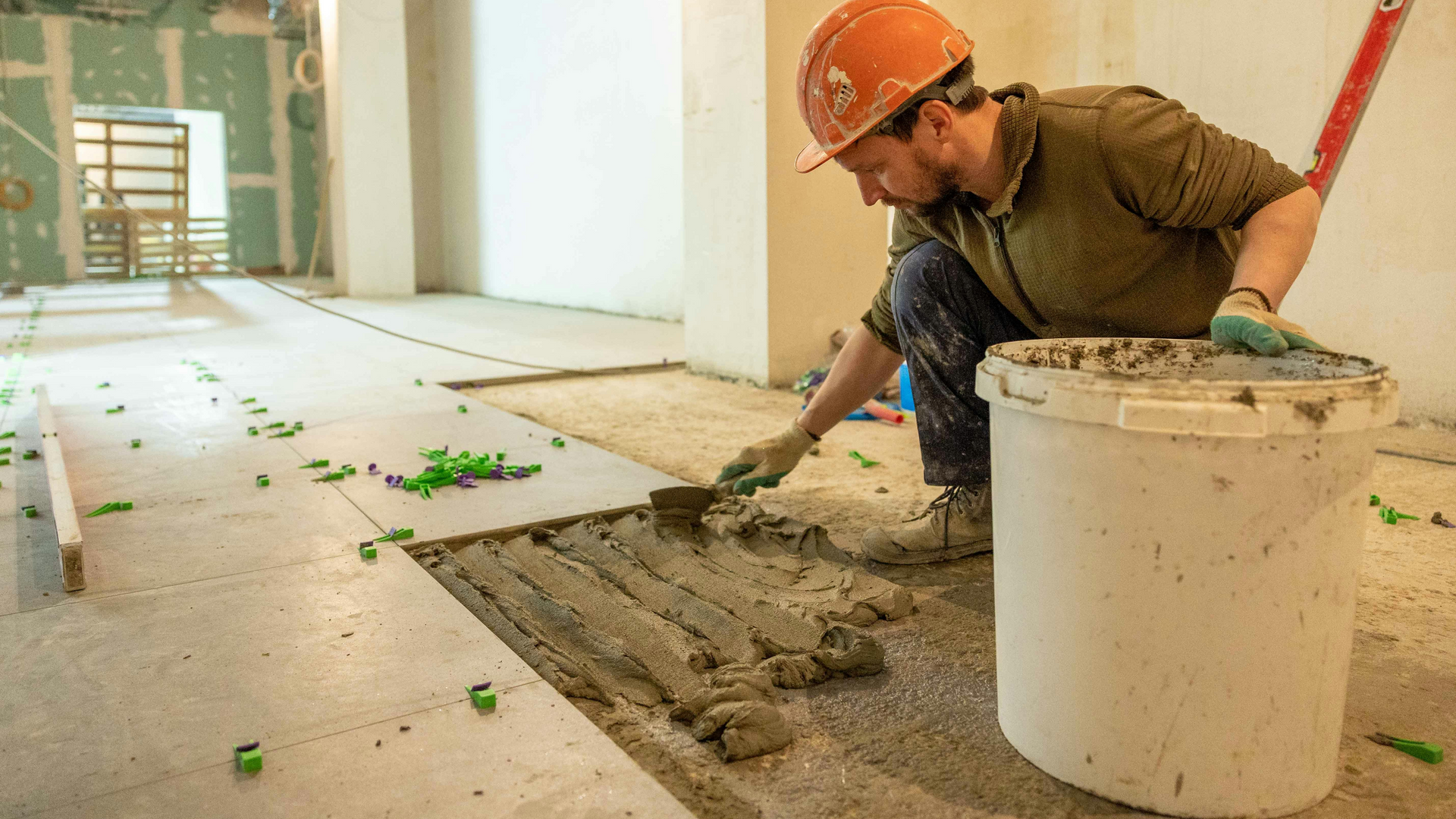 A man is laying tiles on a floor in a room.