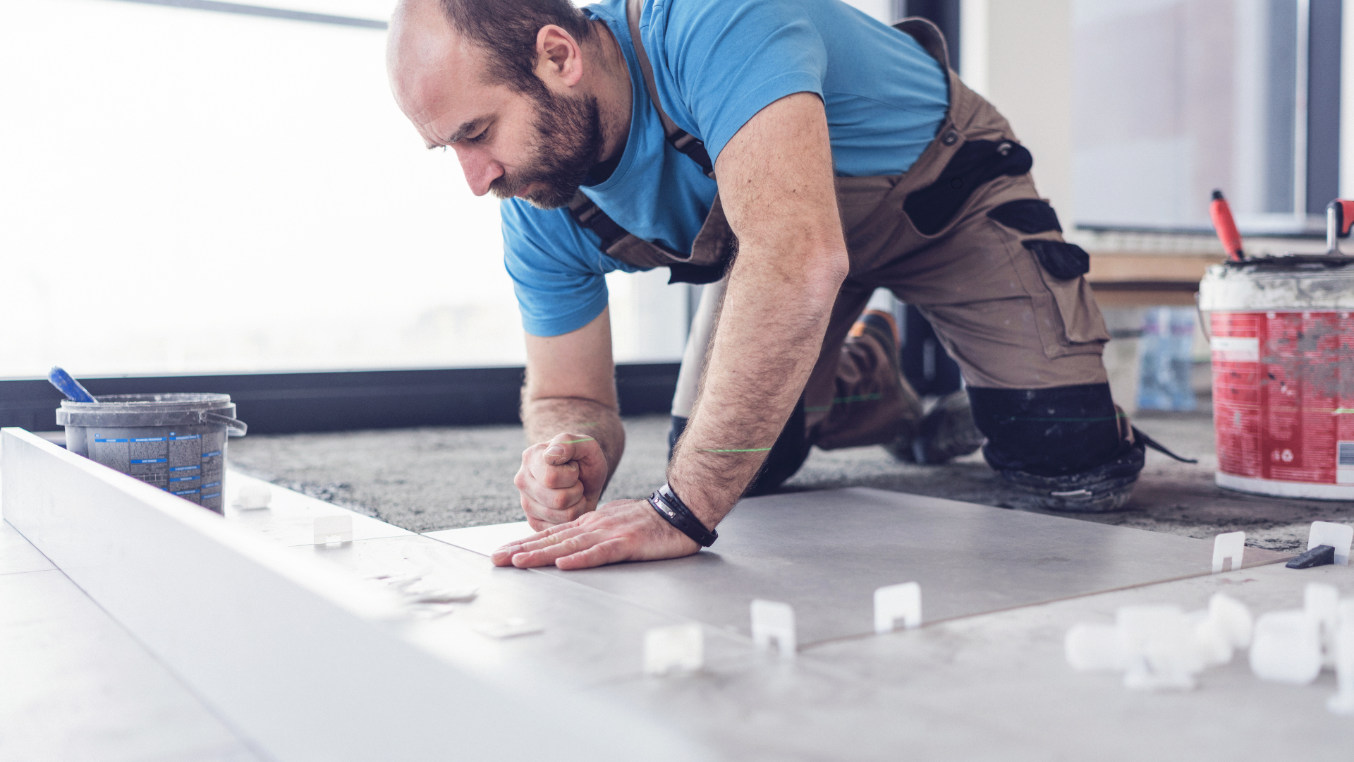 A man is kneeling on the floor while installing a tile floor.