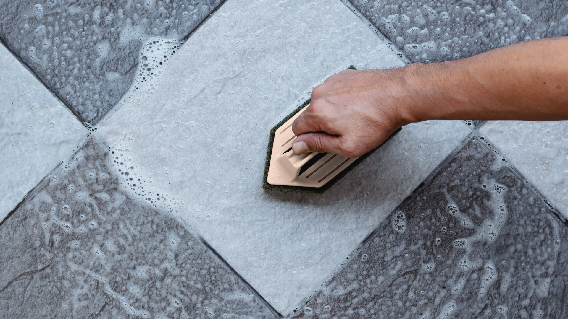 A person is cleaning a tile floor with a sponge.