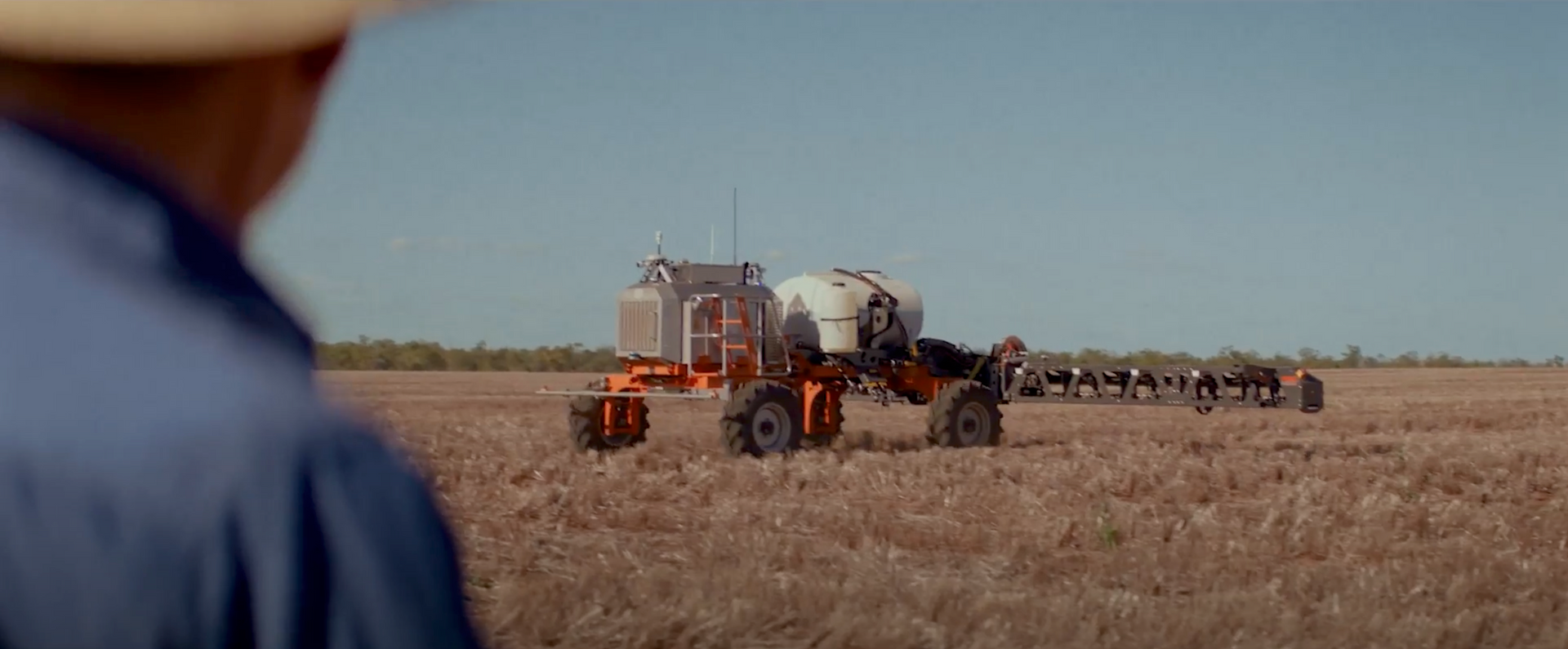 A man in a cowboy hat is looking at a tractor in a field.