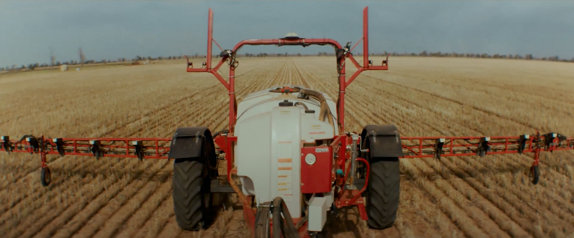 A red and white tractor is spraying a field.