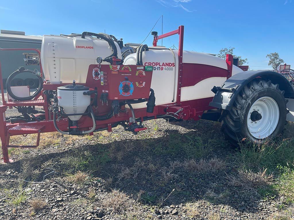 A red and white sprayer is parked next to a tractor.