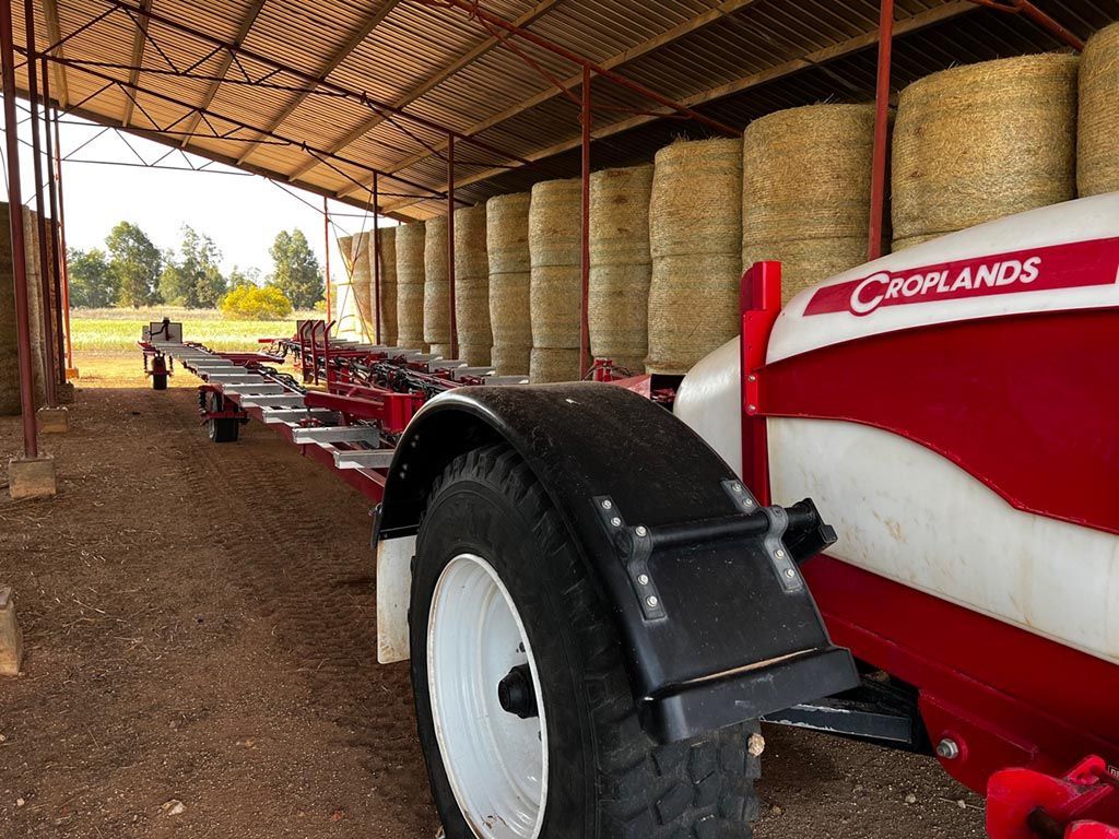 A red and white tractor is parked in a barn filled with hay bales.