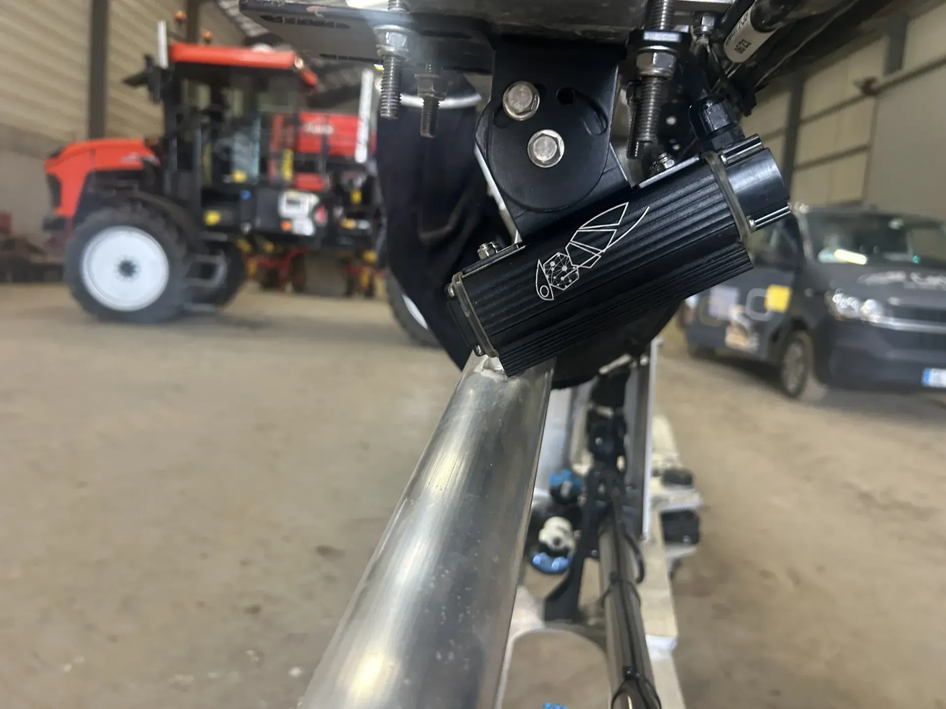 A sprayer is parked in a farm shed with a van in the background.