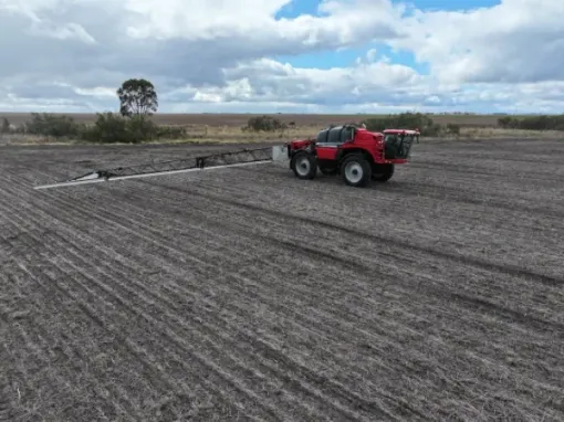 A red tractor is plowing a field on a cloudy day.