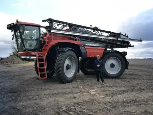 A man is standing in front of a large red tractor in a field.