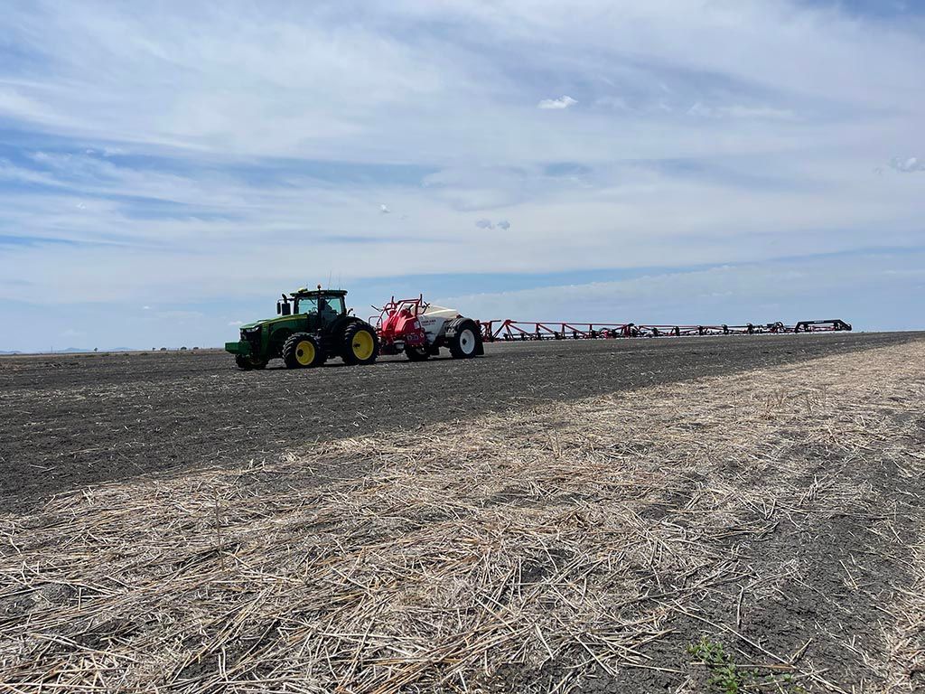 A tractor is plowing a field with a sprayer attached to it.