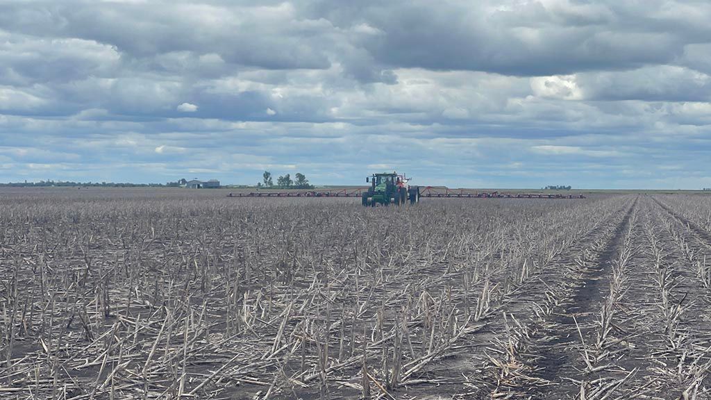 A tractor is plowing a large field on a cloudy day.