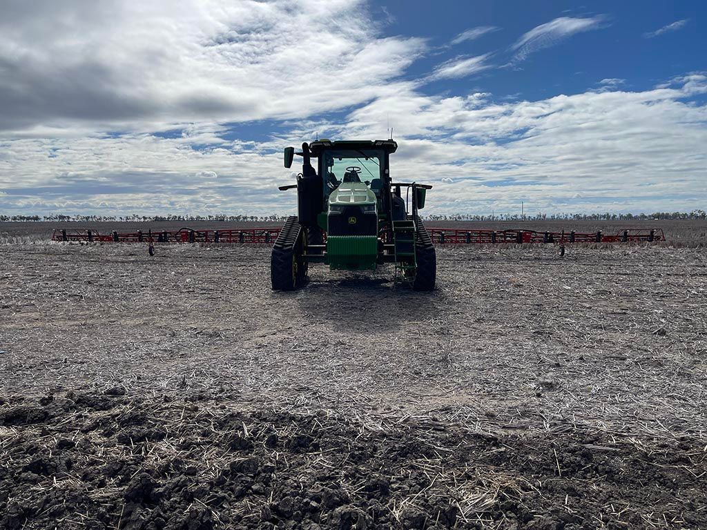 A green tractor is plowing a field on a cloudy day.