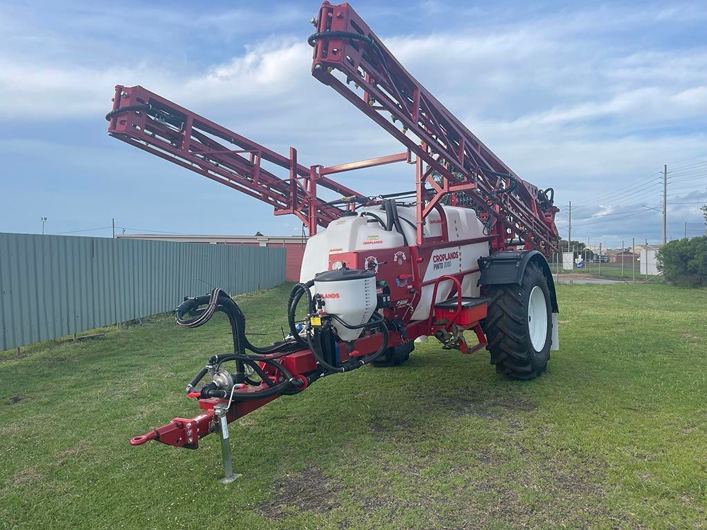 A red and white sprayer is parked in a grassy field next to a fence.