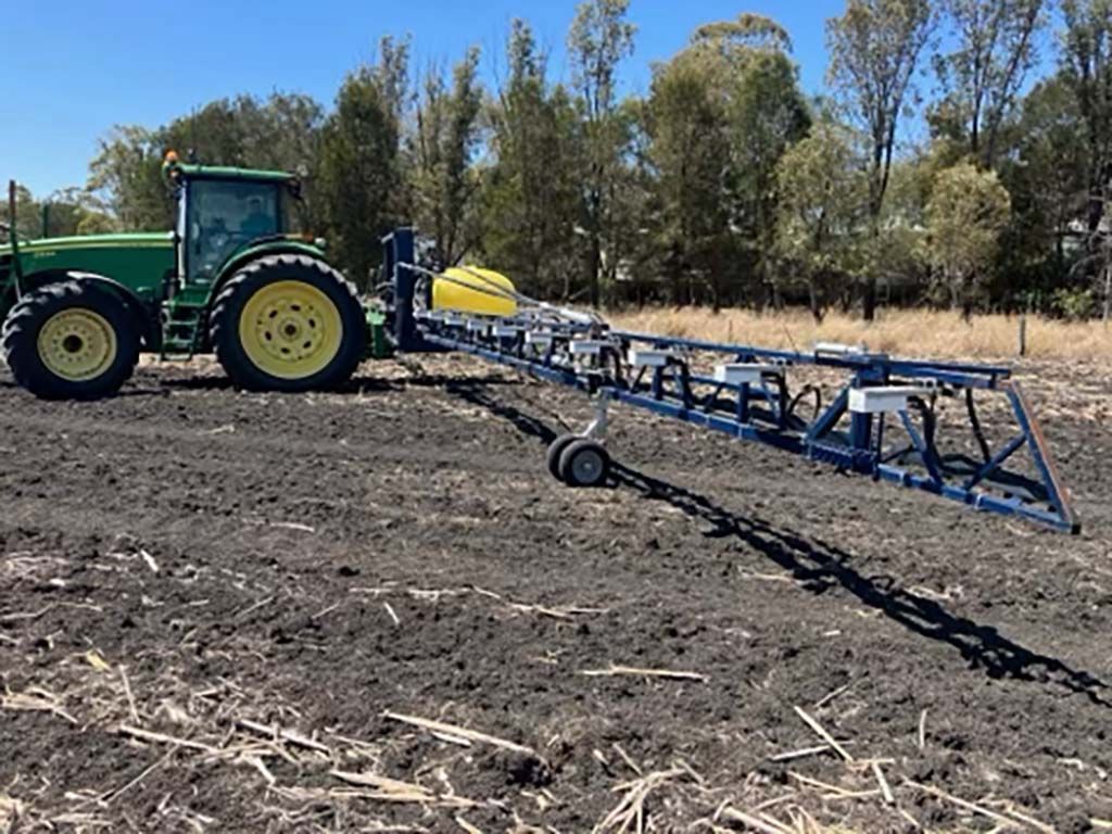 A green tractor is plowing a field with a sprayer attached to it.