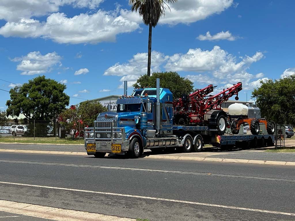 A blue semi truck is driving down the road with a tractor on the back.