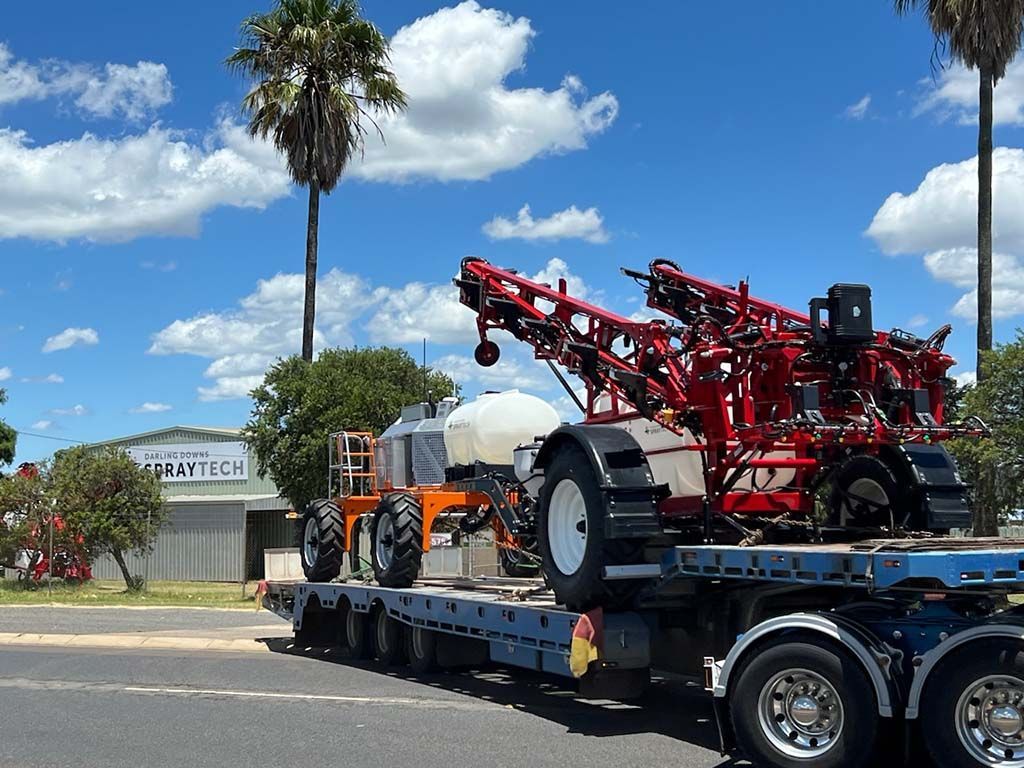 A truck is carrying a large red tractor on a trailer.