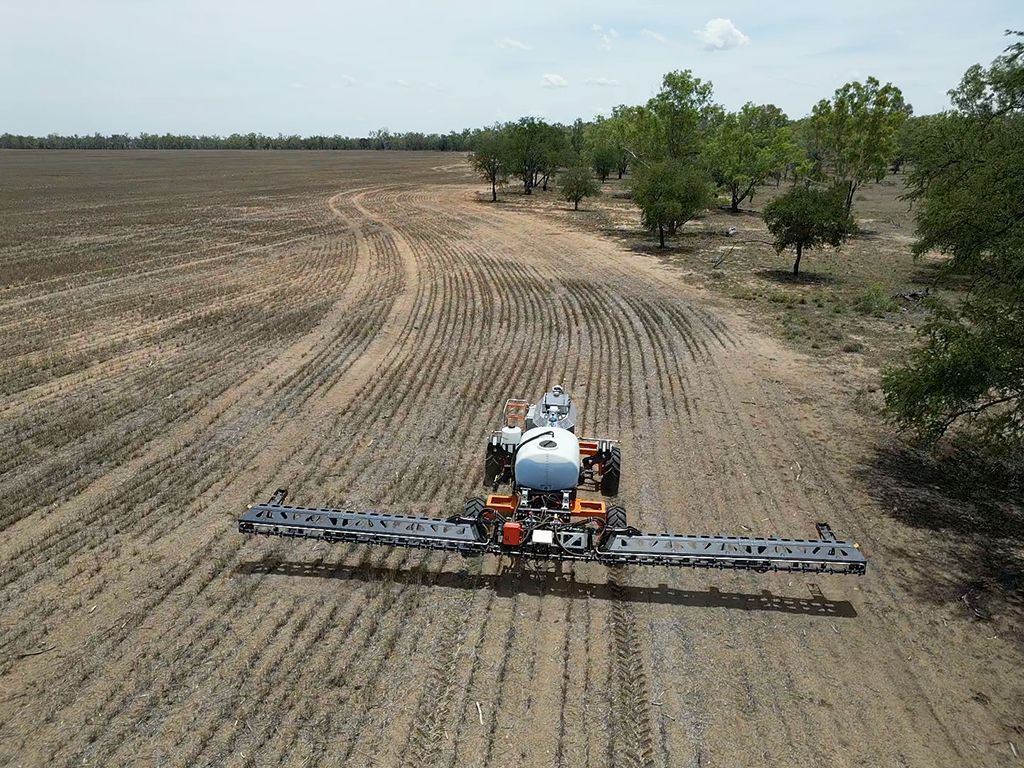 An aerial view of a tractor spraying a field with a sprayer.