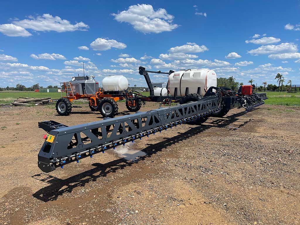 A sprayer is parked in a dirt field next to a tractor.