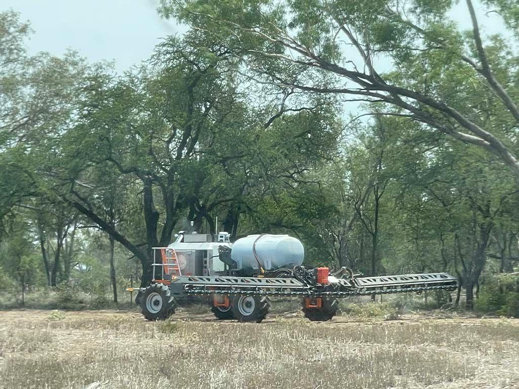 A tractor is spraying a field with trees in the background