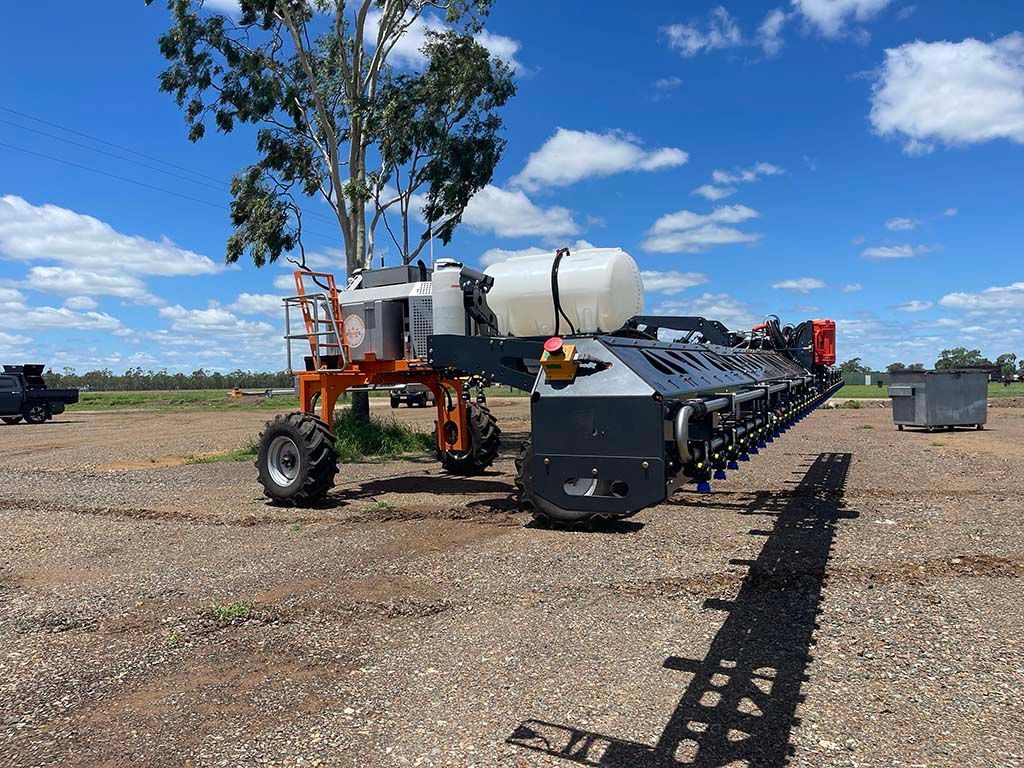 A large tractor is parked in a gravel lot next to a tree.