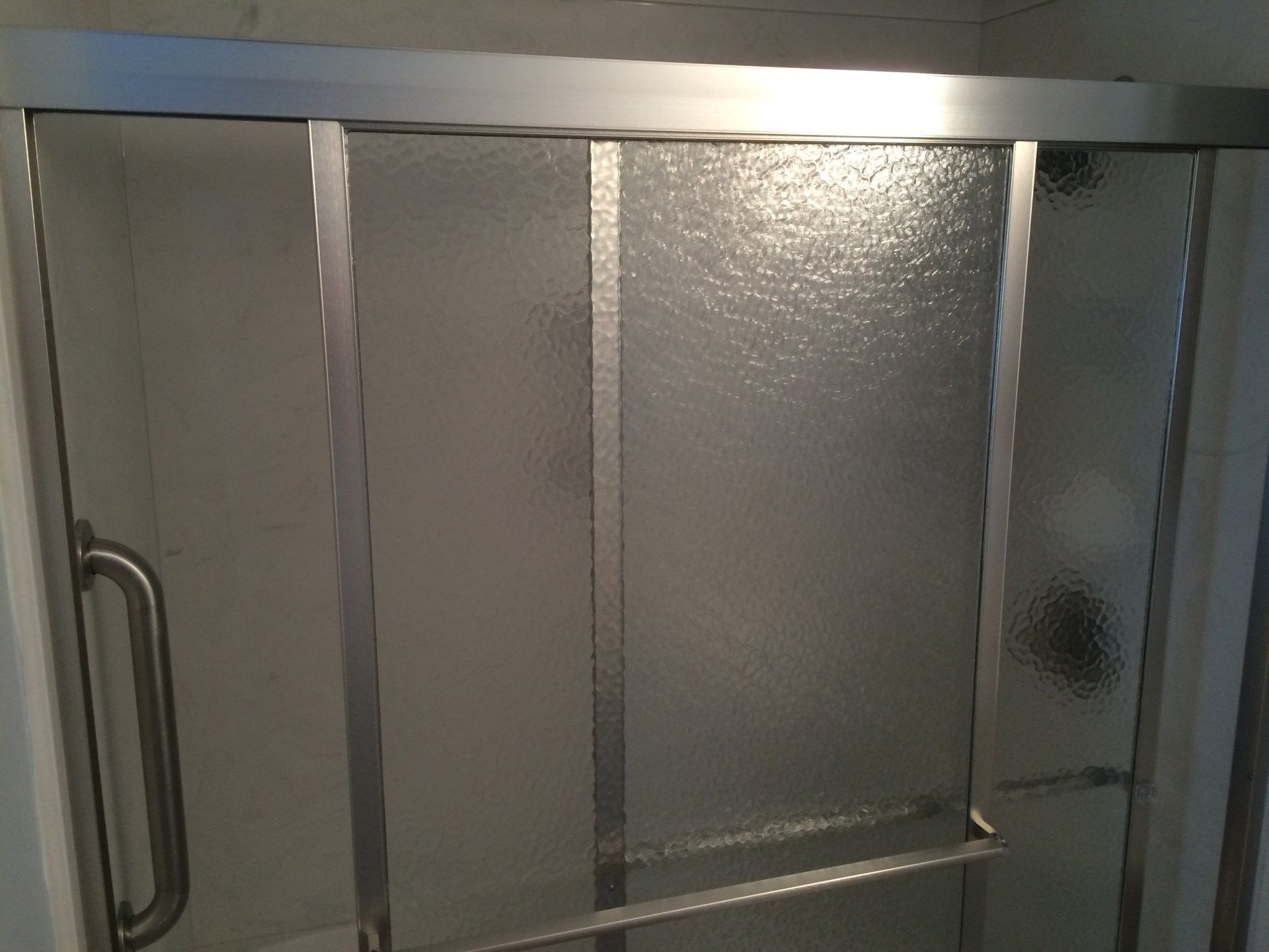 A sliding glass shower door in a bathroom with a handle