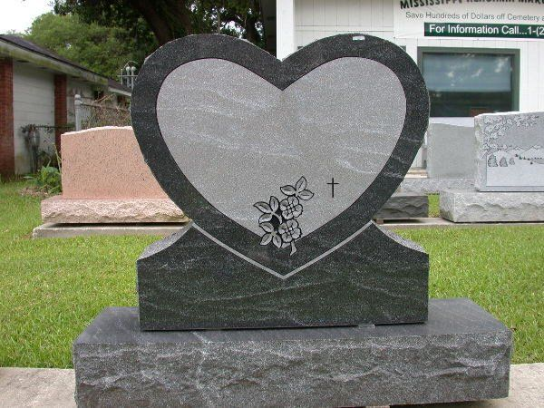 A heart shaped gravestone with a cross and flowers on it