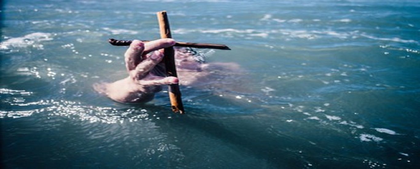 A person is holding a cross in the water.