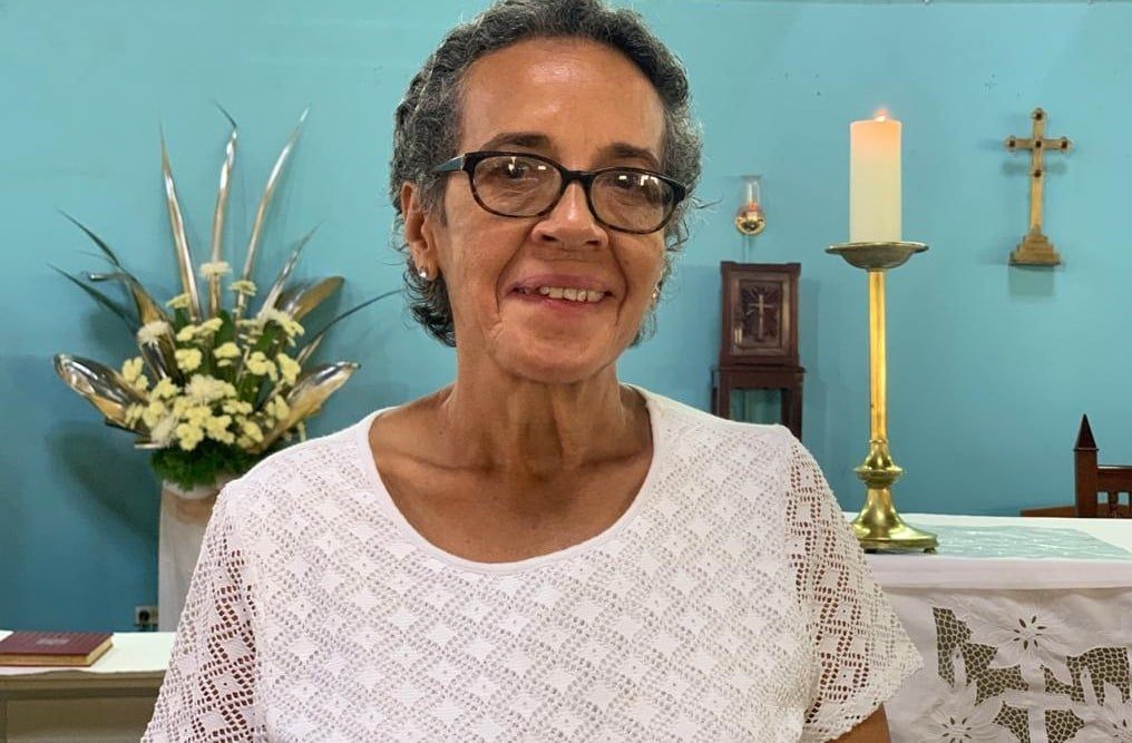 A woman wearing glasses is smiling in front of a candle in a church.
