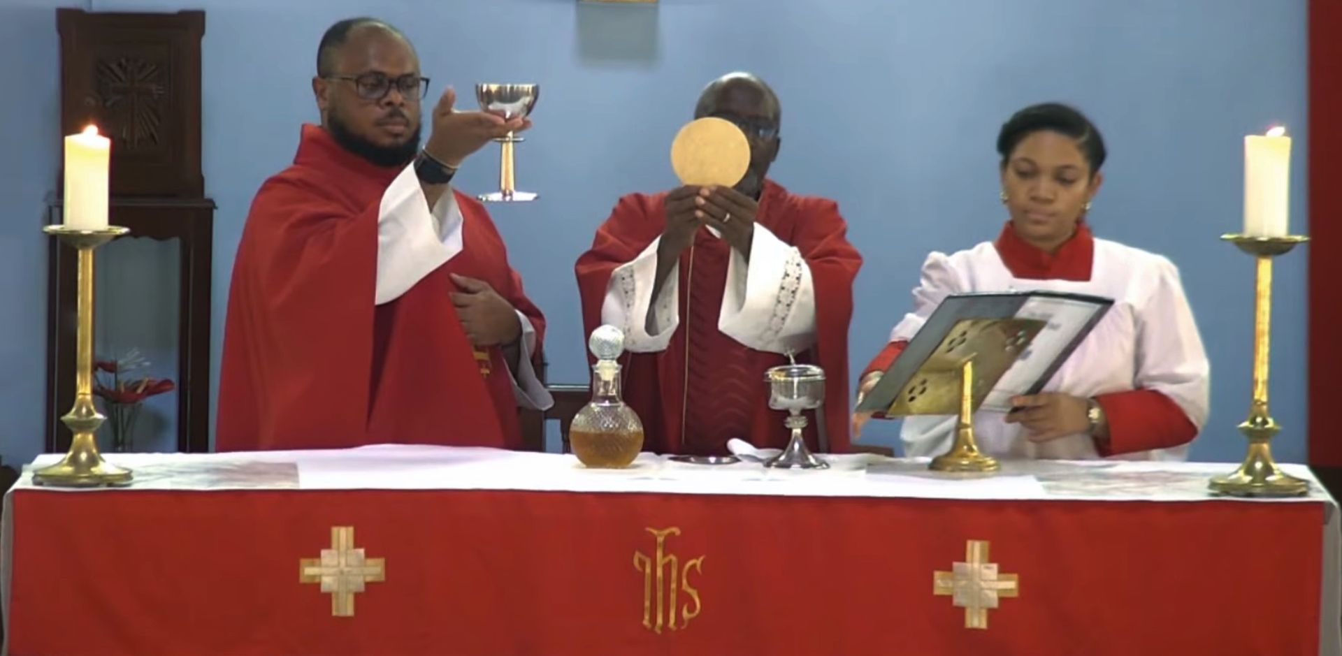 A group of priests are standing at an altar holding a chalice and a host.