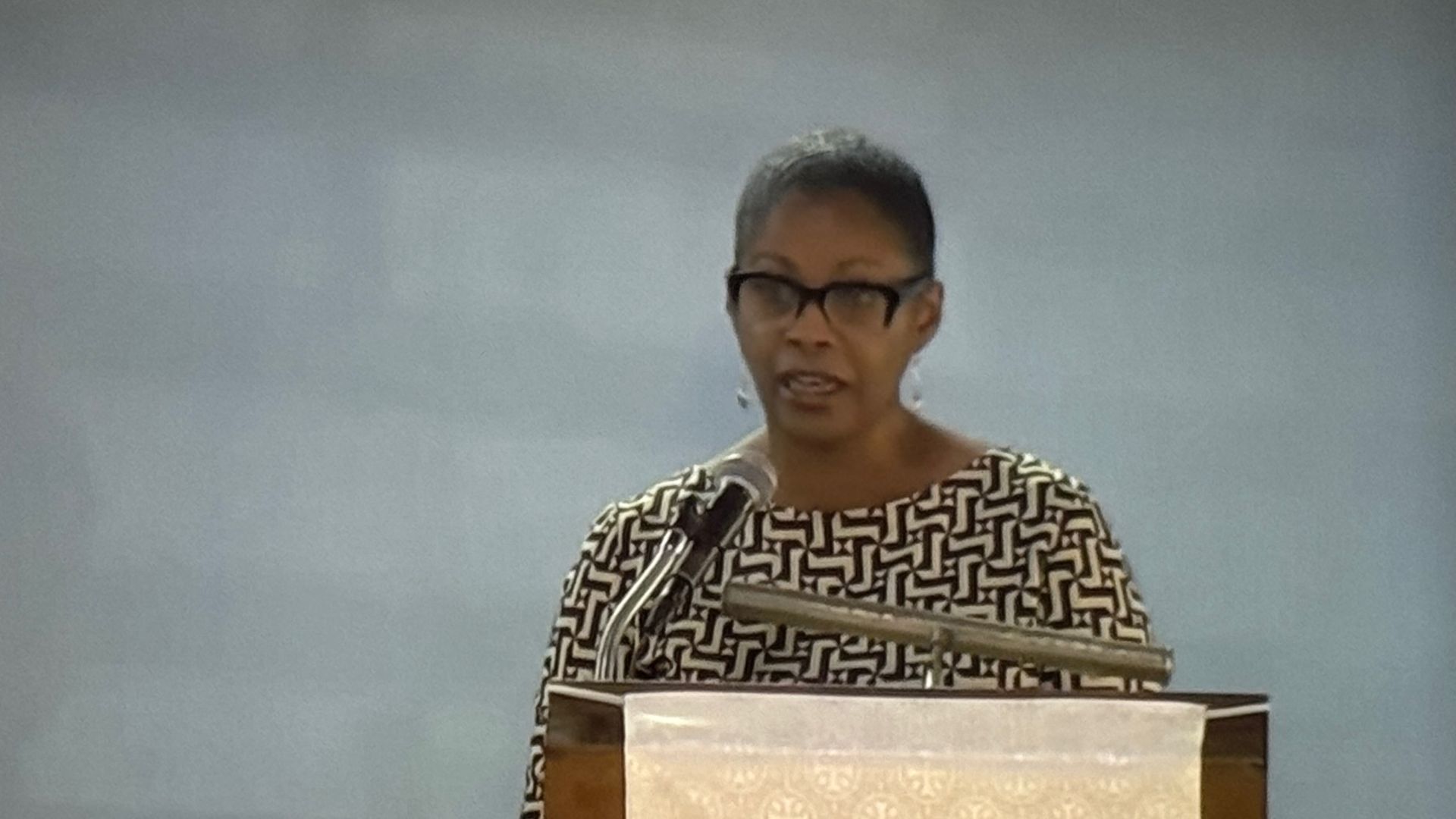 A woman is standing at a podium speaking into a microphone.