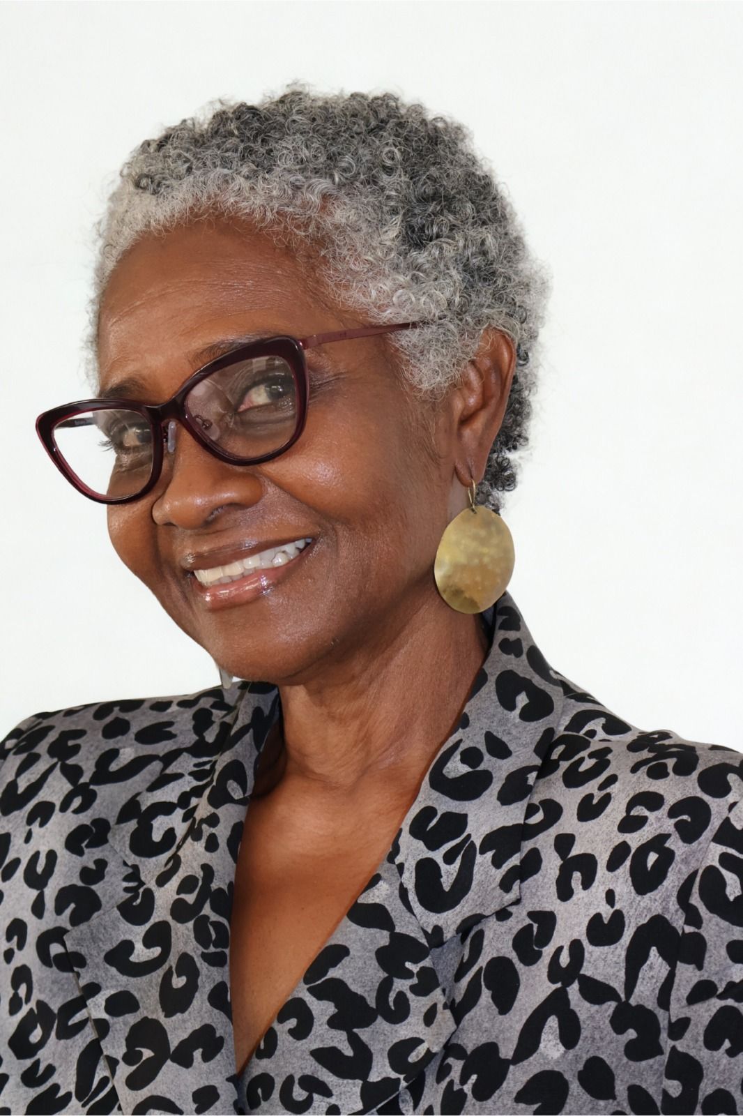 Woman with short gray hair, wearing glasses, and leopard-print blazer, smiling.
