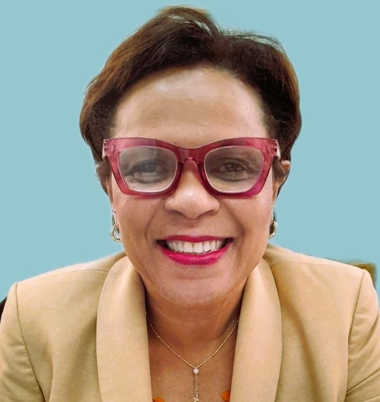 A woman wearing glasses and a tan jacket is smiling