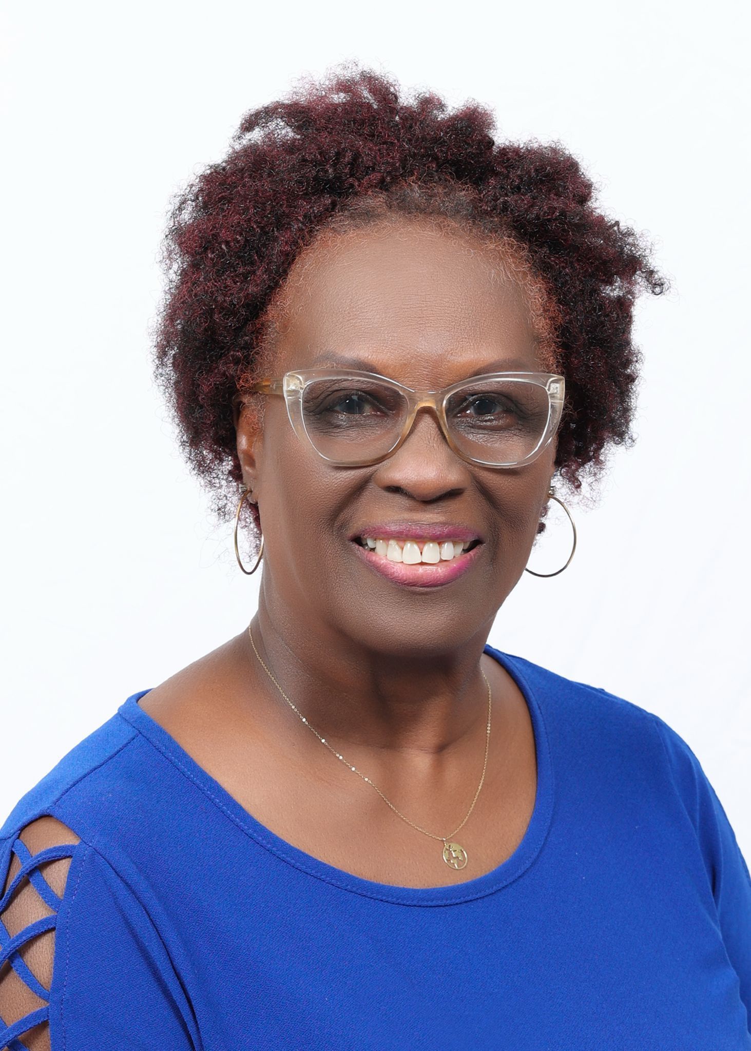 Woman with glasses and red curly hair smiling in a blue shirt.
