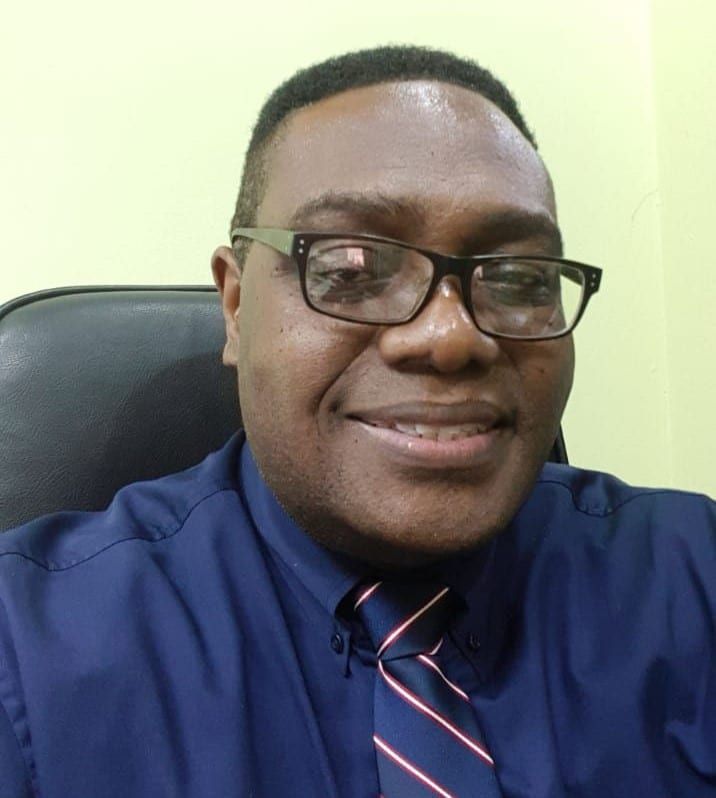 A man wearing glasses and a blue shirt and tie is smiling for the camera.