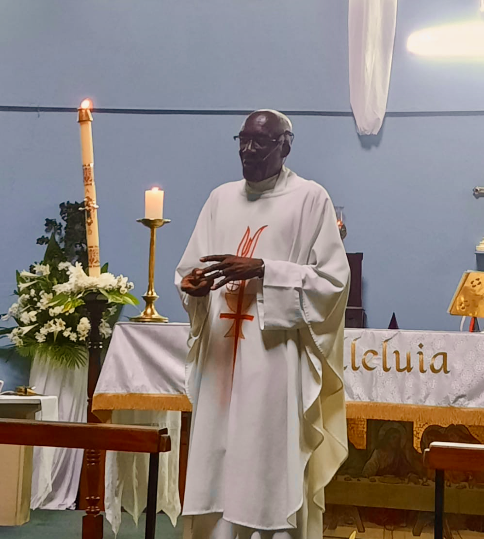 A man in a white robe stands in front of a table with the word leluia on it