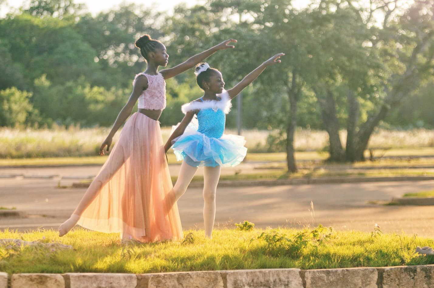Two young ballerinas are dancing in a park.