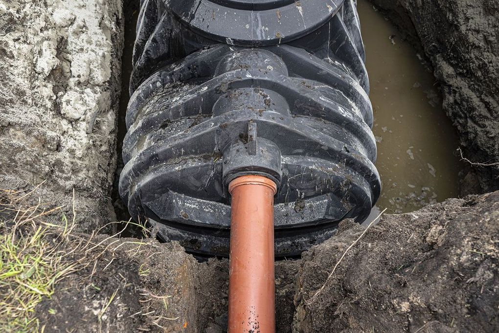 A red pipe is connected to a septic tank in the dirt.