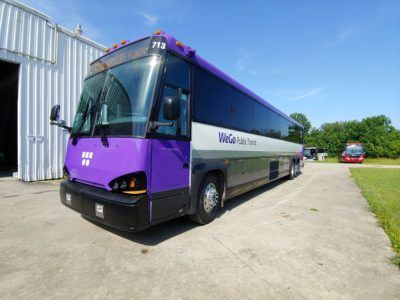 A purple and white bus is parked in front of a building.