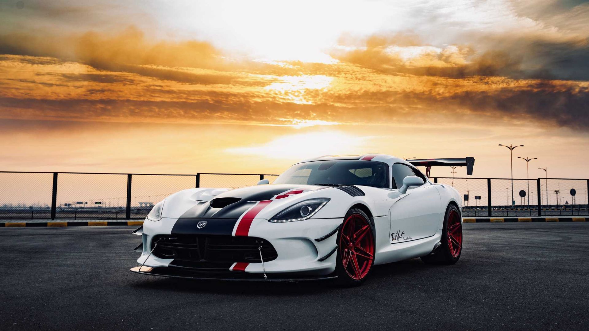 A white dodge viper is parked in a parking lot at sunset.