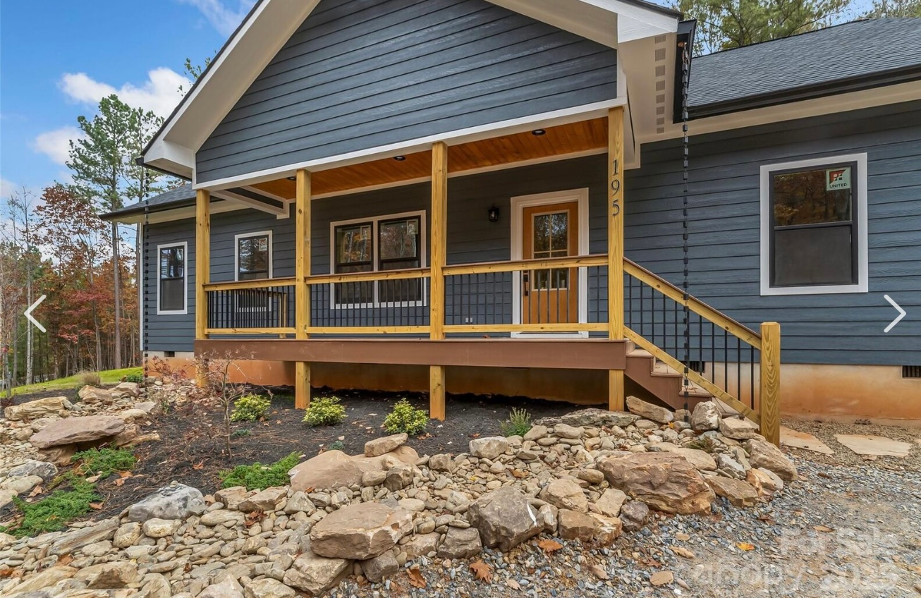 Blue house with a porch and steps, surrounded by rocks and a partially landscaped yard.