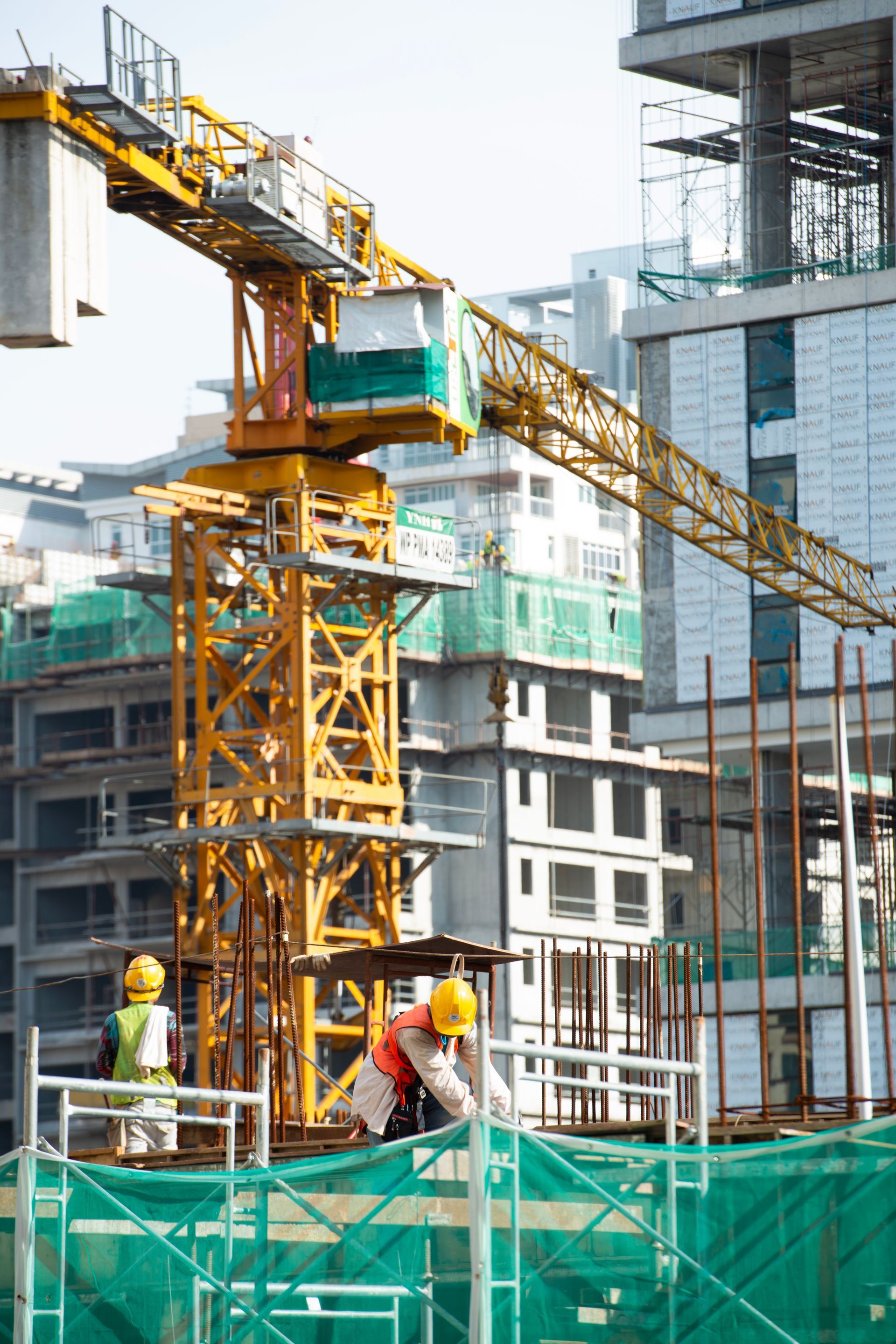 Construction workers on a building site with a yellow crane and unfinished high-rise buildings.