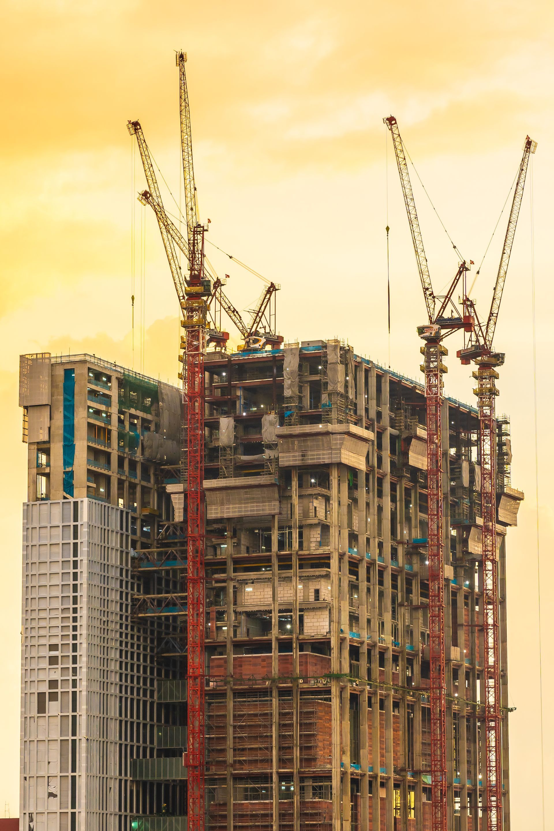 Construction site with tall buildings and several cranes against a golden sky.