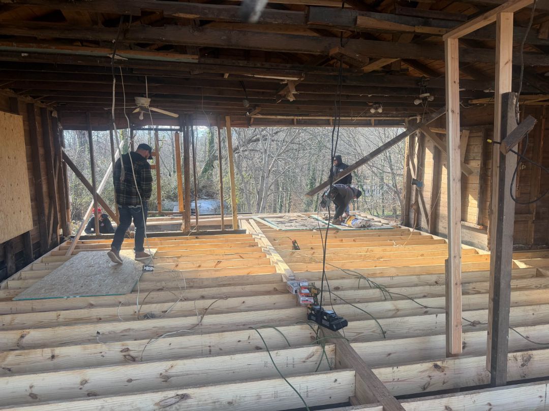 Two people work inside a partially constructed building. Wooden beams form the floor and walls.